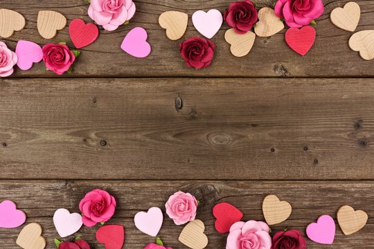 Valentines Day double border of wooden hearts and paper roses against a rustic wood background with copy space.