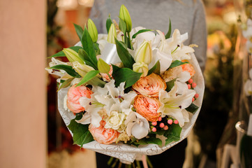 woman holds a bouquet lilies, orchids, pion-shaped roses in wrapping paper
