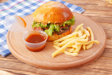 Hamburger with sauce and fried potato on wooden plate