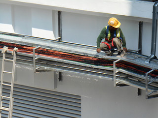 Electrical contractor installing electrical cable tray at the construction site. Working at height wearing proper safety gear. 