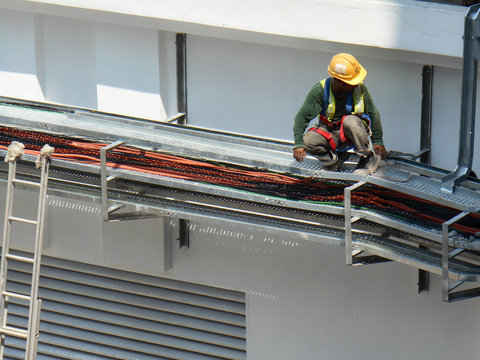Electrical contractor installing electrical cable tray at the construction site. Working at height wearing proper safety gear. 