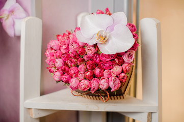 bouquet in the shape of heart with roses and orchid lies on a white chair