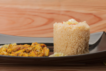 Fried chicken meat and couscous on black plate on wooden table