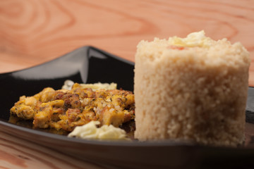 Fried chicken meat and couscous on black plate on wooden table