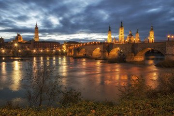 The Cathedral-Basilica of Our Lady of the Pillar and Stone bridge at the night in Zaragoza on the Ebro River, Spain.