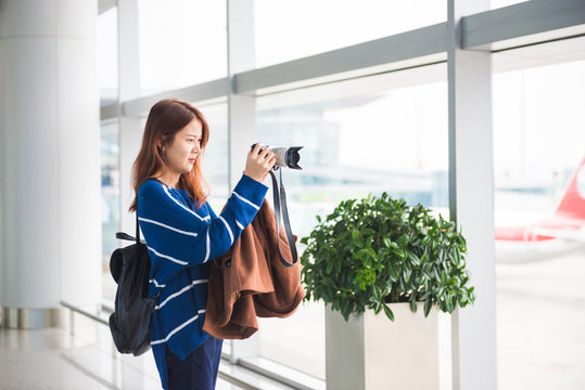 Traveler young asian woman with backpack taking a photo with her digital camera in airport.