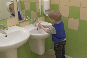 A boy washes his hands in the sink in a public place alone