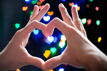 hands of woman in heart shape gesture with heart shape bokeh