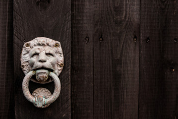 Dark black wooden background with lion shaped door knocker and copy space to the right.