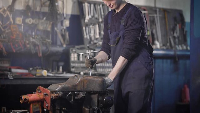 automotive technician is twisting by wrench a cover of old dirty car engine in a workshop of car-service