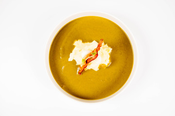 Cream of sorrel and green vegetables soup with quail egg, sour cream, mashed potatoes and crispy bacon on a white background