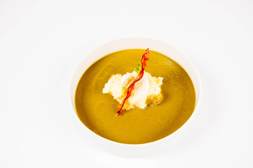 Cream of sorrel and green vegetables soup with quail egg, sour cream, mashed potatoes and crispy bacon on a white background