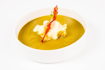 Cream of sorrel and green vegetables soup with quail egg, sour cream, mashed potatoes and crispy bacon on a white background
