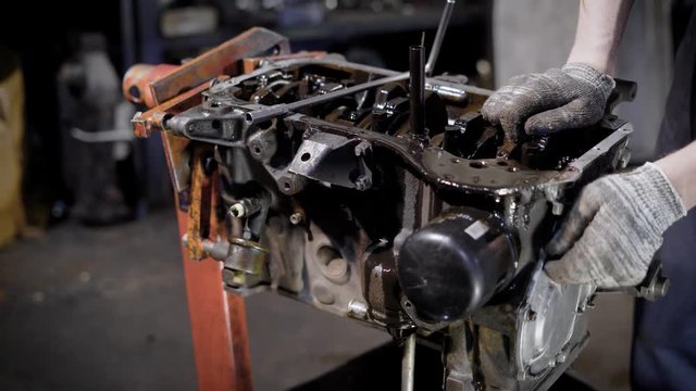 motor technician is disassembling old dirty car engine, taking out details, in an auto-service, close-up