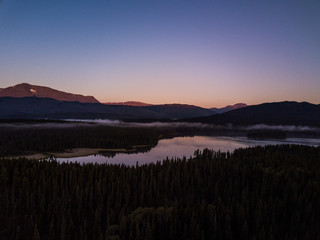 Fototapeta premium Mountain glow coming from the mountain in the background. Clouds and fog are seen above the lake early in the morning. 