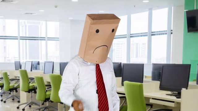 Stressful unknown businessman with paper bag on his head, standing in the office room while thinking idea and scratching head.