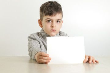 Studio portrait of young boy holding white blank paper