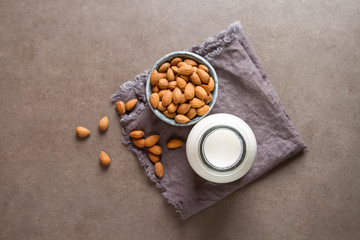 Dairy alternative milk. Almond milk in a glass bottle and fresh nuts over a gray background, selective focus. Clean eating, dairy-free, vegan, vegetarian, allergy-friendly, healthy food concept