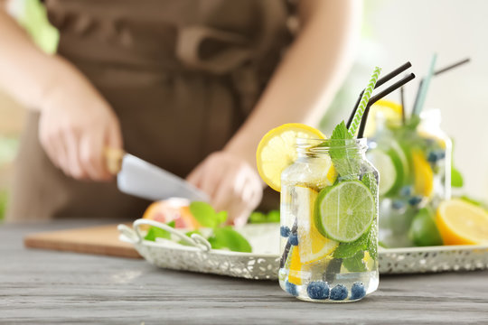 Mason jar of infused water with fruits and blurred woman on background