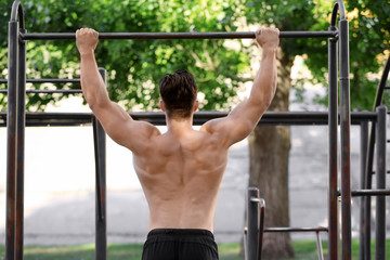 Handsome young man doing chin ups outdoors