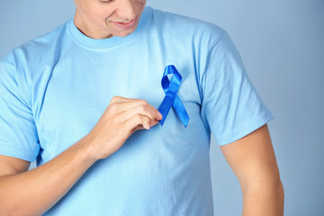 Young man wearing t-shirt with blue ribbon on color background, closeup. Prostate cancer awareness concept