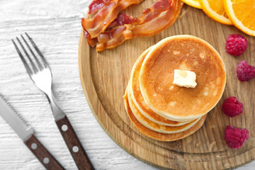 Tasty breakfast with pancakes, bacon and fruits on wooden board