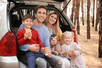 Young couple with their little children having lunch while sitting in car trunk