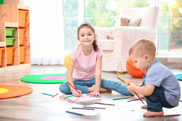 Fototapeta premium Happy little girl and toddler boy drawing with colored pencils on floor in bright playroom, early childhood education and creative development