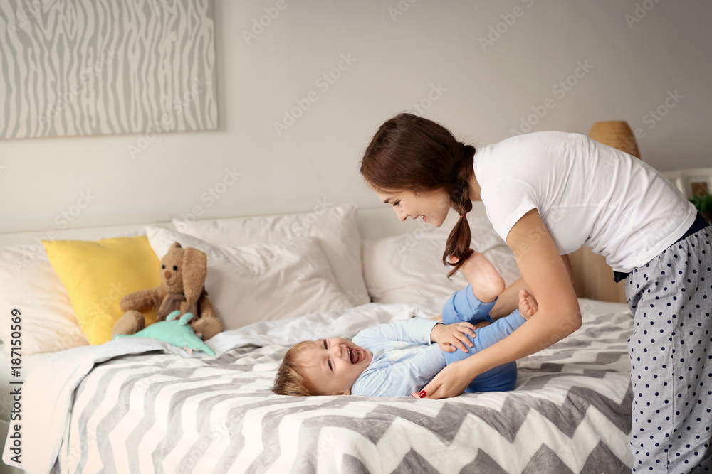 Wall mural beautiful young woman tickling her baby on bed at home