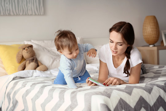 Beautiful young woman reading to her baby on bed at home