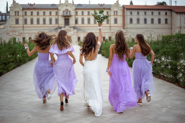 happy bride with the bridesmaids are running playful. View from the back. Wedding concept - obrazy, fototapety, plakaty