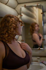 Redheaded young woman looking at herself in the mirror in the bathroom
