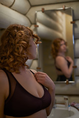Fototapeta premium Redheaded young woman looking at herself in the mirror in the bathroom