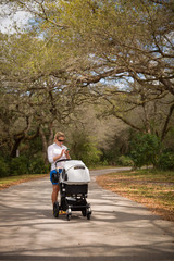 Young woman walking in the park with baby stroller. Happy mother with child in the carriage. Girl with a pram outdoors in the big park.