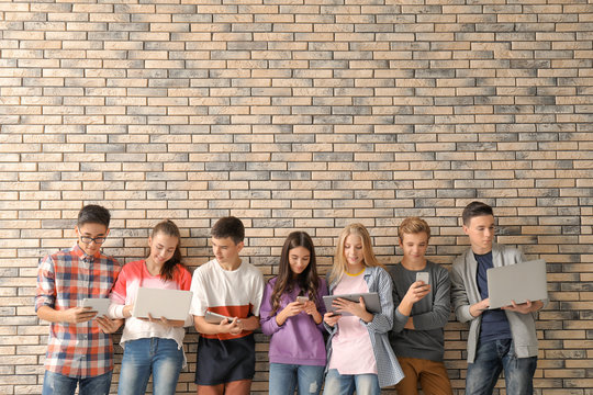 Group of cool teenagers with modern devices near brick wall