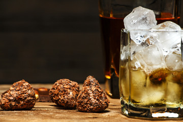 A glass of cognac or whiskey on a rustic table with chocolate and truffles.