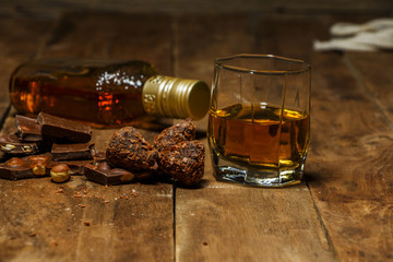 A glass of cognac or whiskey on a rustic table with chocolate and truffles.