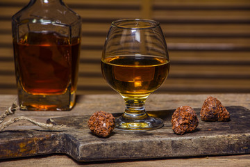 A glass of cognac or whiskey on a rustic table with chocolate and truffles.