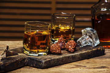 A glass of cognac or whiskey on a rustic table with chocolate and truffles.