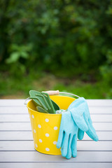 Yellow bucket with garden tools and Rubber blue safety gloves on the table in the garden. Hand...
