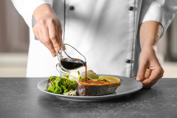 Chef pouring sauce onto tasty rainbow trout steak in kitchen