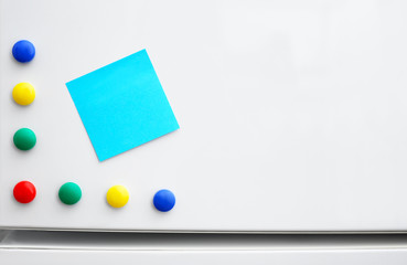 Empty sticky note and colorful magnets on refrigerator door, closeup