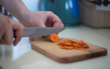 Chef is cutting carrot on a wooden cutting board with sharp knife