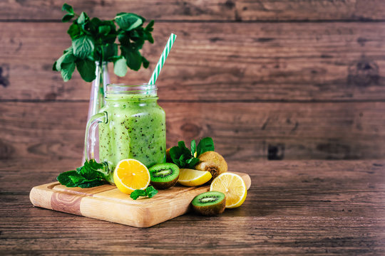Delicious kiwi smoothie with mint in mason jar on table against dark wooden background. Healthy lifestyle concept