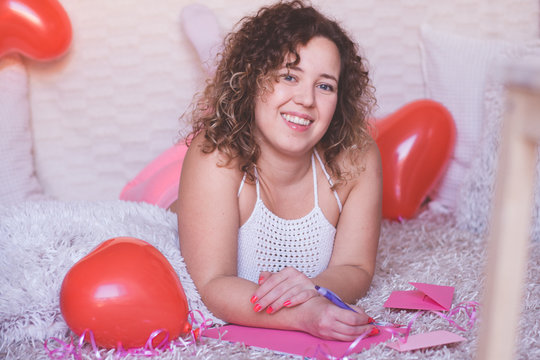 Young beautiful woman smiling and writing a letter for Valentines Day on pink paper.