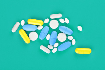 Assorted pharmaceutical medicine pills, tablets and capsules on green background