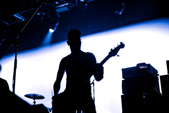 Rock band performs on stage. Guitarist plays solo. silhouette of guitar player in action on stage in front of concert crowd.