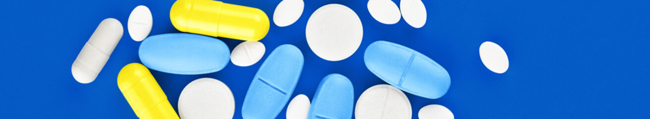 Assorted pharmaceutical medicine pills, tablets and capsules on blue background