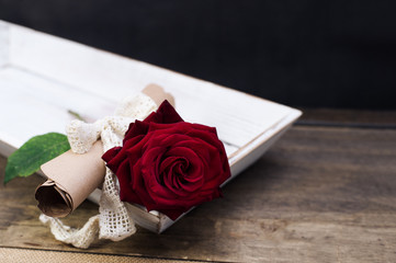 surprise for St. Valentine's Day on a table: red rose and a message on papyrus vintage paper with a...