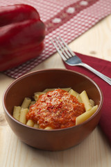 penne alla crema di peperone rosso e parmigiano su tavola in abete con forchetta e tovagliolo rosso.
